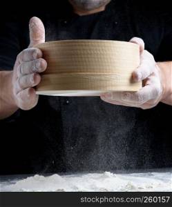 round wooden sieve in male hands, the cook sifts the flour