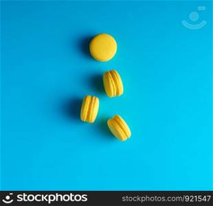 round yellow baked macarons with cream lie on a blue background, top view
