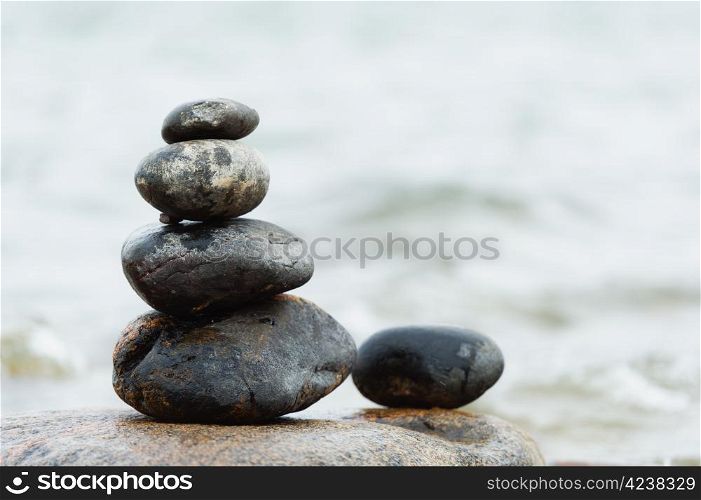Rounded stones are set-up to pile, focus on stones, sea on the background.