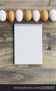 row brown white eggs near blank notepad wooden desk