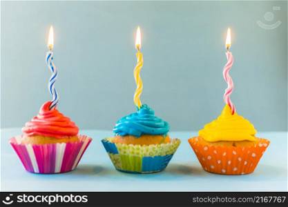 row cupcakes with burning candles blue backdrop