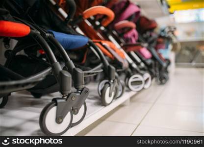 Row of baby strollers on shelf in store, nobody, goods for newborns. Pushchair variety in shop. Row of baby strollers on shelf in store, nobody