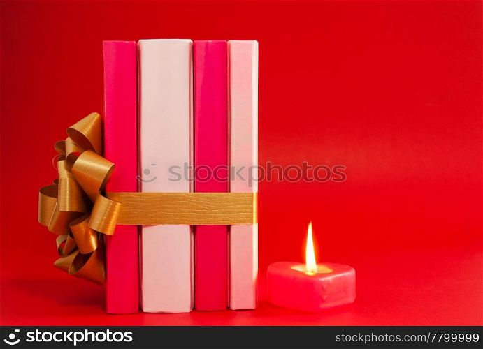 Row of books tied up with ribbon and burning candle over red background