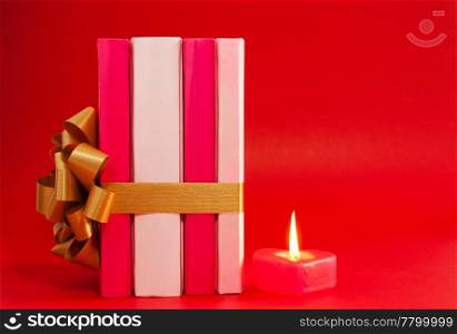 Row of books tied up with ribbon and burning candle over red background