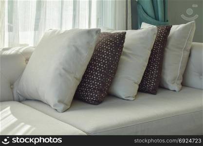 Row of brown and white pillows on beige sofa next to the window