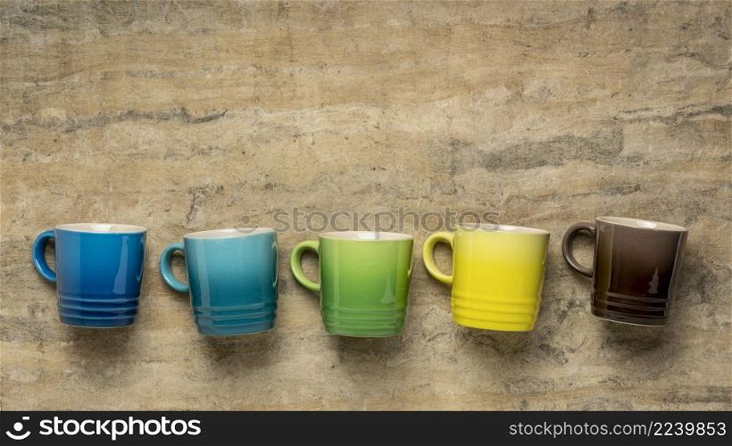 row of colorful stoneware coffee cups against textured handmade bark paper with a copy space