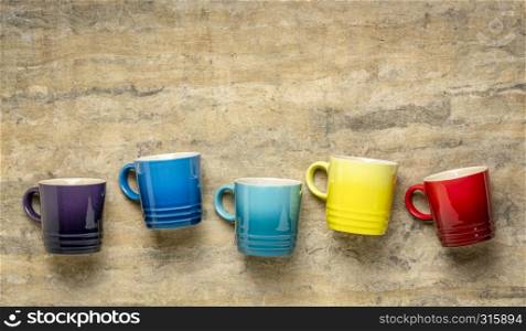 row of colorful stoneware coffee cups against textured handmade bark paper with a copy space