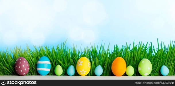 Row of Easter Eggs in fresh green grass over blue sky background