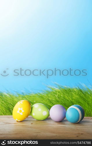 Row of Easter eggs on wooden plank over fresh green grass background