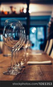 Row of empty wine glasses on a wooden table, served for wine tasting event. Bar or shop interior, subdued light, lovely atmosphere, selective focus, film grain effect