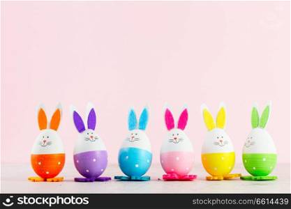 Row of funny easter bunnies of colored eggs on pink background with copy space. Easter scene with colored eggs