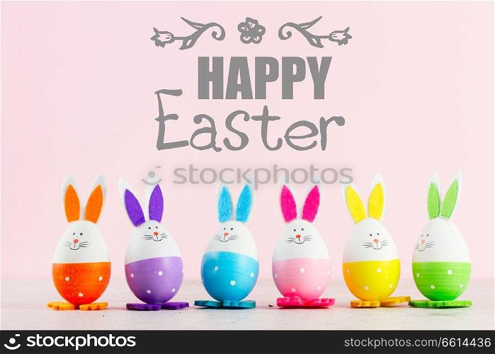 Row of funny easter bunnies of colored eggs on pink background with happy Easer greetings. Easter scene with colored eggs