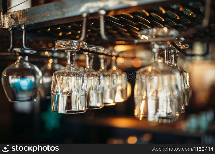 Row of glasses hanging on the bar counter closeup, nobody. Barman equipment, bartending utensil, barkeeper tools. Row of glasses hanging on the bar counter closeup