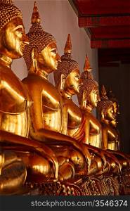 Row of golded sitting Buddha statues in Buddhist temple Wat Pho, Bangkok, Thailand. Low point of view, focus on 3rd one from the left