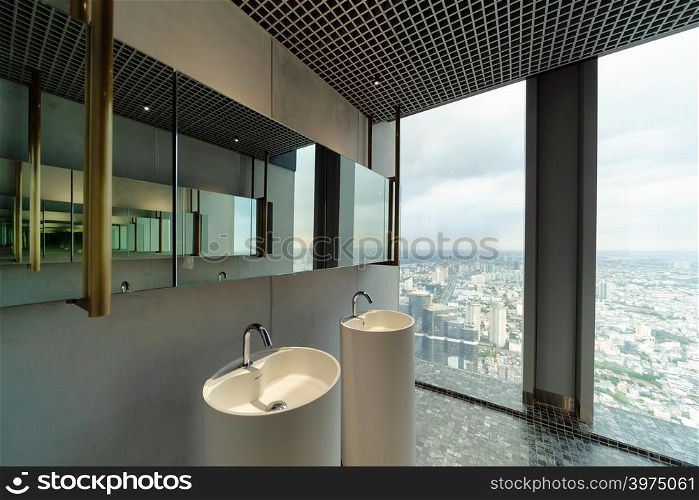Row of modern white ceramic wash basin in public toilet with cityscape background, restroom in restaurant or hotel or shopping mall, interior decoration design