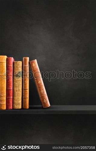 Row of old books on black shelf. Vertical background scene. Row of old books on black shelf. Vertical background