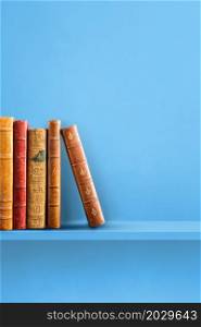 Row of old books on blue shelf. Vertical background scene. Row of old books on blue shelf. Vertical background