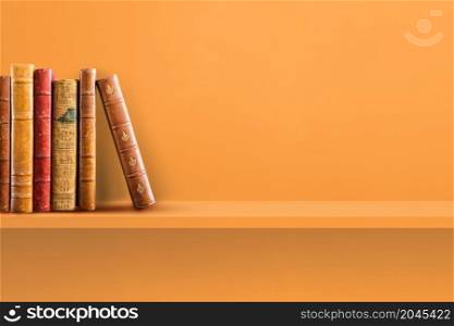 Row of old books on orange shelf. Horizontal background scene. Row of old books on orange shelf. Horizontal background