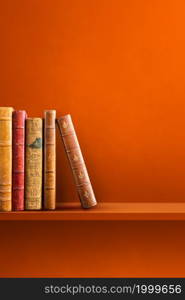 Row of old books on orange shelf. Vertical background scene. Row of old books on orange shelf. Vertical background