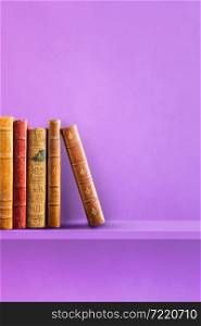 Row of old books on purple shelf. Vertical background scene. Row of old books on purple shelf. Vertical background