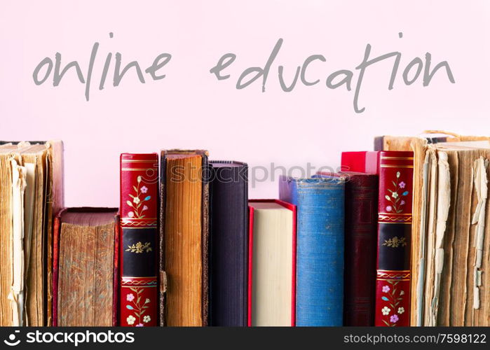 Row of old books on wooden shelf on pink background, online education concept. Pile of old books