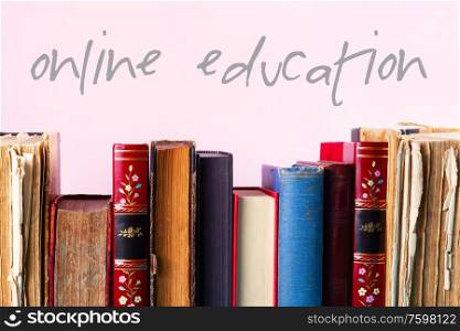 Row of old books on wooden shelf on pink background, online education concept. Pile of old books