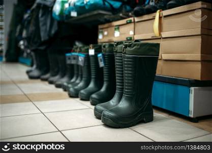 Row of rubber boots in fishing shop, nobody. Equipment and tools for fish catching and hunting, accessory choice on showcase in store. Row of rubber boots in fishing shop, nobody