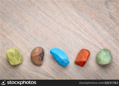 row of semiprecious colorful polished gemstones against grained wood with a copy space
