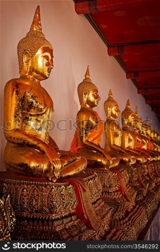 Row of sitting Buddha statues in Buddhist temple Wat Pho, Bangkok, Thailand. Low point of view