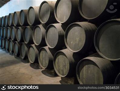 Row of stacked wooden wine barrels for sherry aging. Row of stacked oak casks or barrels along wall of winery for aging sherry or port. Row of stacked wooden wine barrels for sherry aging