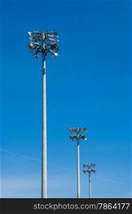 Row of three industrial stadium flood light towers on clear blue sky.