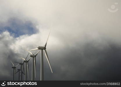 Row of turbines at wind farm again cloudy gray sky.