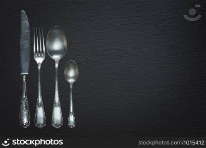 Row of vintage knife, fork and spoons are on a black slate surface, with copy-space