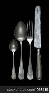 Row of vintage pewter knife, fork and spoons are isolated on a black background