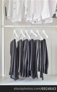 row of white shirts and black pants hanging in wooden wardrobe