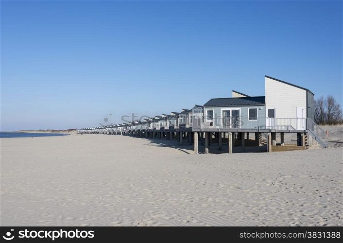 row of wooden beach houses for vacation on the white beach sand near the blue water sea in holland with the dunes as background