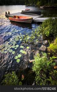 Rowboat tied to dock on beautiful lake at rocky shore with aquatic plants. Ontario, Canada.
