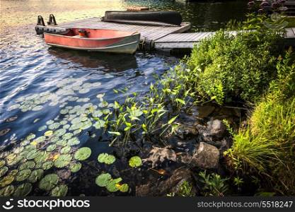 Rowboat tied to dock on beautiful lake at rocky shore with aquatic plants. Ontario, Canada.