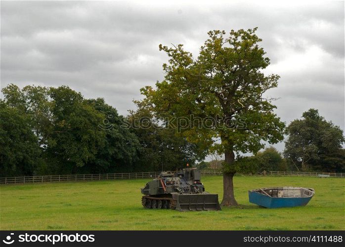 Rowing boat and tank under tree in field