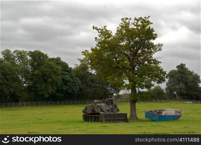 Rowing boat and tank under tree in field