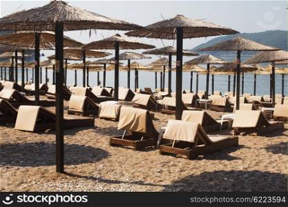Rows of brown wooden lounge chairs and straw beach umbrellas on sea beach in the morning. Budva, Montenegro