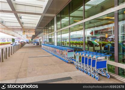 Rows of luggage carts by the Singapore airport entrance, taxi cabs reflecting in glass facade