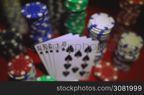 Royal flush on cards and poker chips on red casino table.