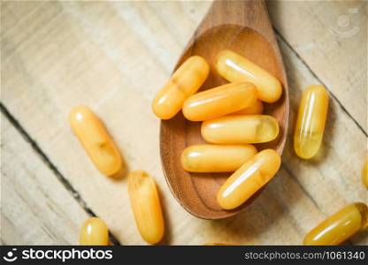 Royal jelly capsules in wooden spoon and wood table background / Yellow capsule medicine or supplementary food from nature for health