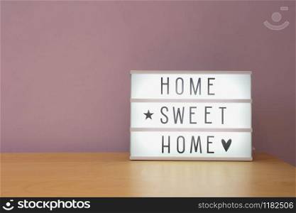 &rsquo;Home sweet home&rsquo; text in lighbox on wooden shelf, modern retro decoration purple wall. &rsquo;Home sweet home&rsquo; text in lighbox on wooden shelf, modern retro decoration