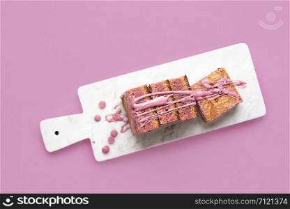 Ruby chocolate dessert in slices displayed on a white cutting board and pink background. Above view of pink chocolate cake. Flat lay of pink brownies