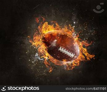 Rugby ball in a fire flames on dark background. Mixed media. American football game concept. Mixed media