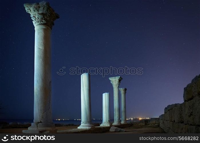 Ruins of ancient city columns under blue night sky with moon and stars