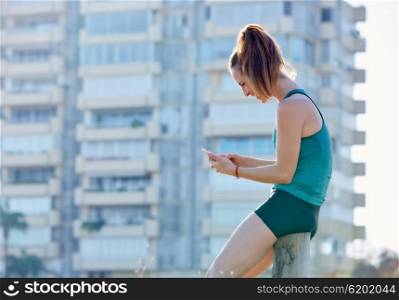 Runner girl having a rest and using smartphone telephone outdoor building park