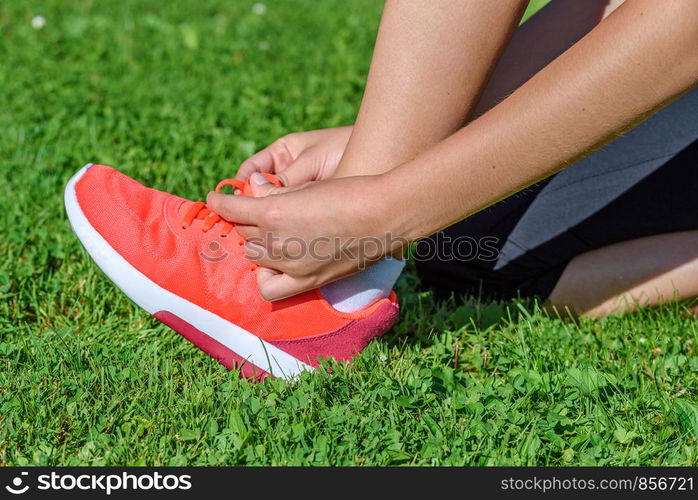 Runner woman kneeling on the grass and tying shoelaces on a sunny day